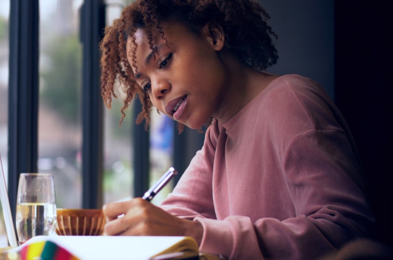 Qual opção é a melhor? | Foto de uma moça concentrada em escrever | Trilha da Conquista | Blog da Tenda