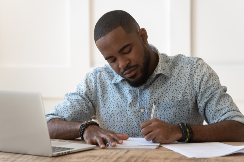 Como contratar um refinanciamento de imóvel? | Foto de um homem escrevendo em um caderno na frente do notebook | Tenda Explica | Blog da Tenda