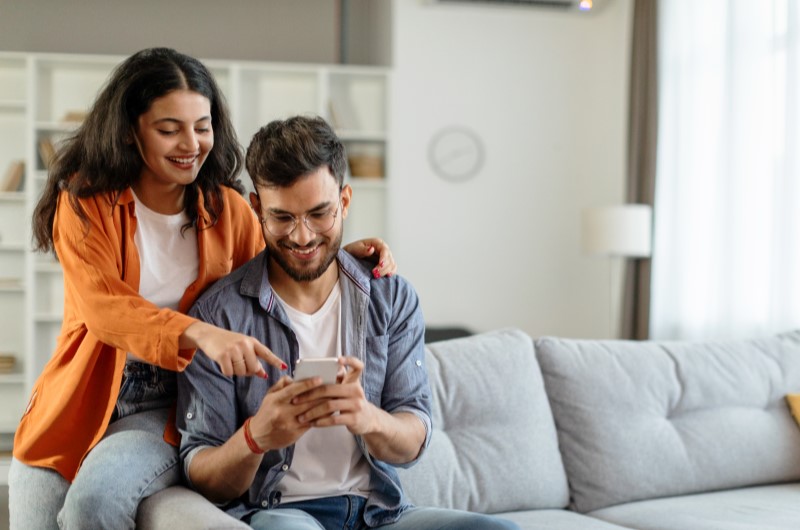 O que saber antes de comprar um apartamento? | Foto de um casal na sala de estar olhando para o celular | Trilha da Conquista | Blog da Tenda