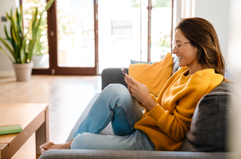 Pagamento via PIX | Foto de uma moça sentada no sofá da sala e usando o celular | Trilha da Conquista | Blog da Tenda