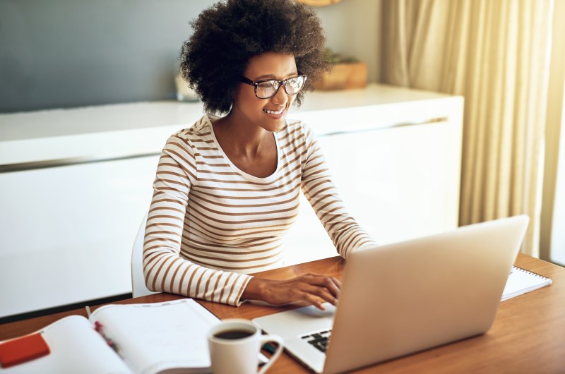Conheça alguns dos bairros de Fortaleza | Foto de uma moça sorridente enquanto usa o notebook | Trilha da Conquista | Blog da Tenda