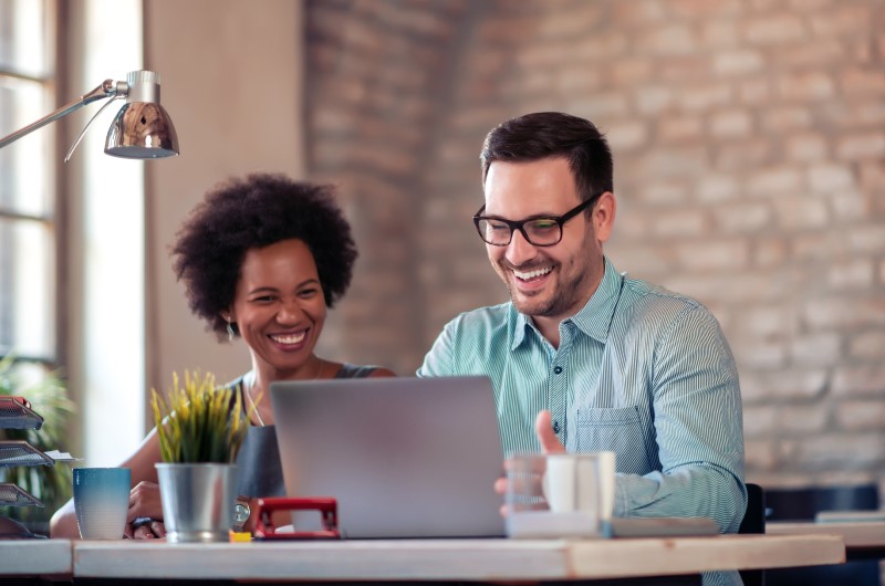 O que é o programa Eu Indico a Tenda? | Foto de duas pessoas sorridentes usando o notebook | Tenda Explica | Blog da Tenda