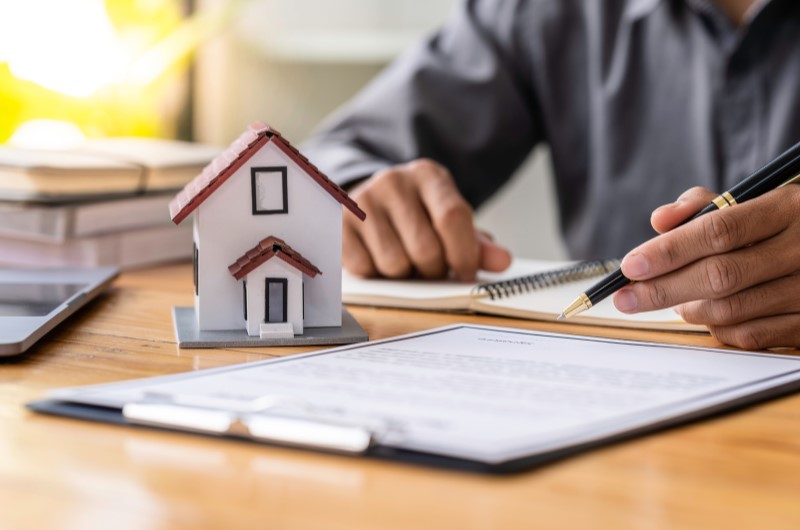 O que é o programa Minha Casa, Minha Vida 2024? | Foto de uma casinha com um documento ao lado e um homem ao fundo | Minha Casa, Minha Vida | Blog da Tenda