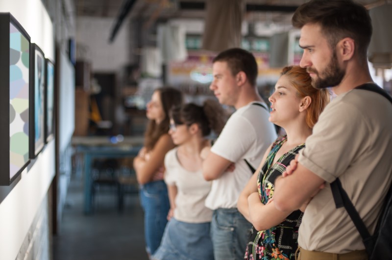 Visite museus | Foto de um grupo de amigos observando uma exposição em um museu | Trilha da Conquista | Blog da Tenda