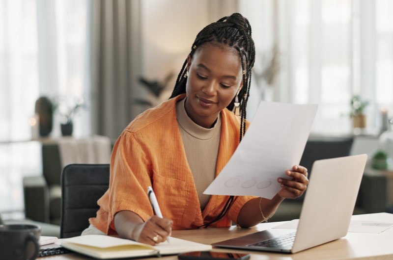 Como o valor oferecido pelo programa pode ser usado? | Foto de uma moça segurando um documento e escrevendo em um caderno | Trilha da Conquista | Blog da Tenda