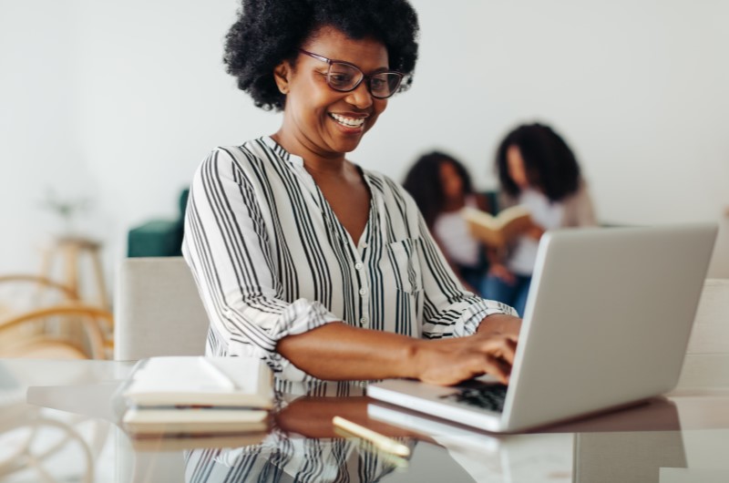 Aproveite o Minha Casa, Minha Vida para comprar um apartamento sem entrada | Foto de um mulher sorridente pesquisando no notebook | Trilha da Conquista | Blog da Tenda