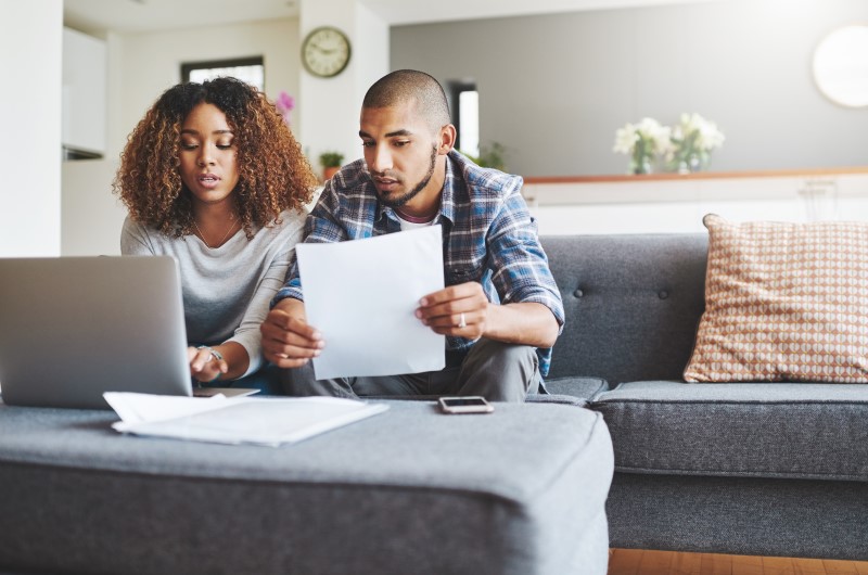 Defina as responsabilidades de cada um | Foto de um casal olhando para o notebook e segurando um documento | Trilha da Conquista | Blog da Tenda