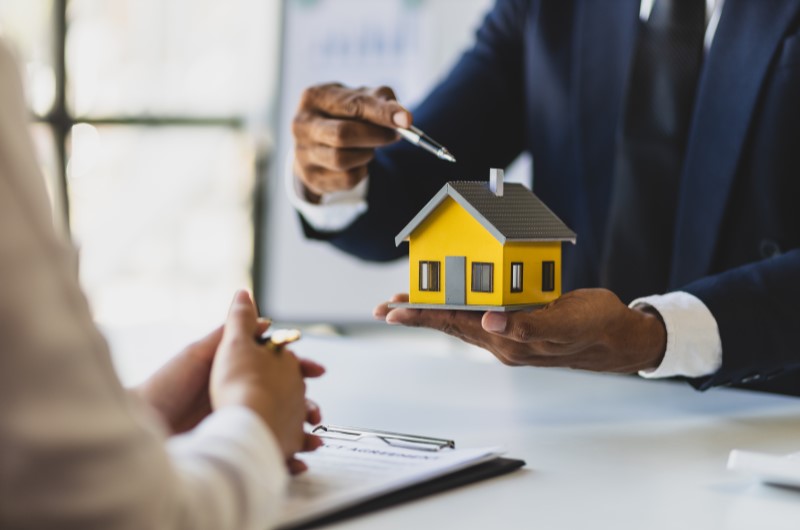 Defina os objetivos e os critérios | Foto de um corretor de imóveis segurando uma casinha e uma caneta | Trilha da Conquista | Blog da Tenda