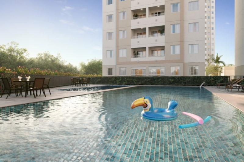 Apartamento com piscina em Salvador | Piscina do condomínio com boia colorida e área de mesas ao fundo, cercada por jardins | Onde Morar | Blog da Tenda 