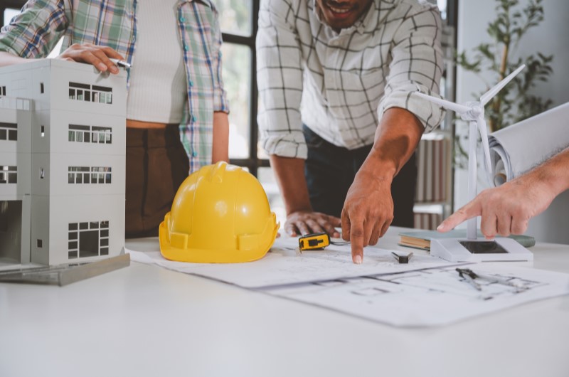 Qual apartamento escolher | Grupo analisando projeto arquitetônico na mesa com capacete e maquete de prédio | Trilha da Conquista | Blog da Tenda 