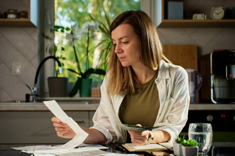 Renegocie as dívidas | Mulher segura faturas e dinheiro na cozinha | Eu Dou Conta | Blog da Tenda