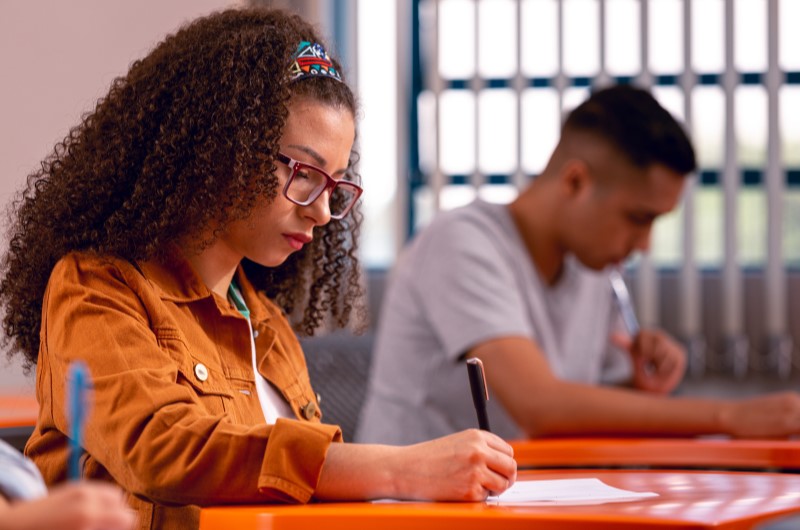 Como participar do programa Pé-de-Meia? | Estudante escrevendo durante uma prova em sala de aula | Trilha da Conquista | Blog da Tenda 