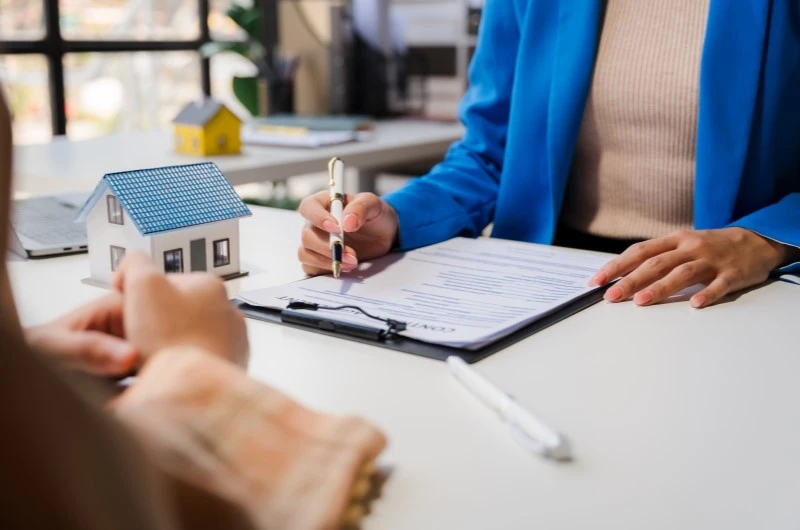 O que é o registro de imóvel | Mulher preenchendo contrato com miniatura de casa sobre a mesa | Trilha da Conquista | Blog da Tenda 