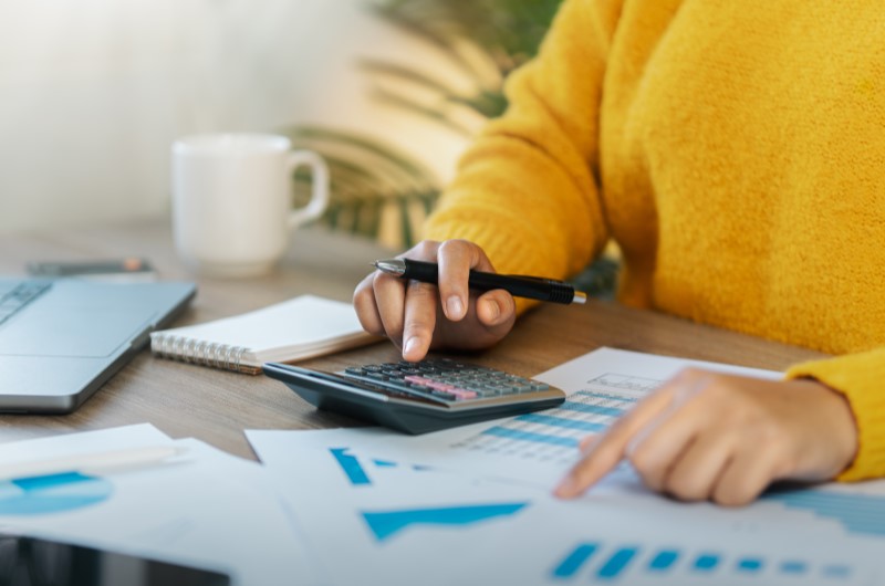 O que é tabela PRICE | Pessoa usando calculadora e analisando gráficos financeiros | Trilha da Conquista | Blog da Tenda 