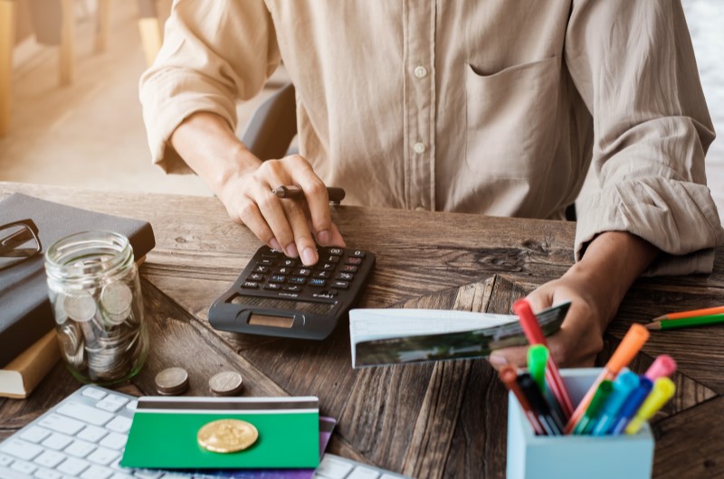 O que são gastos mensais | Pessoa usando uma calculadora e segurando um papel | Eu Dou Conta | Blog da Tenda 