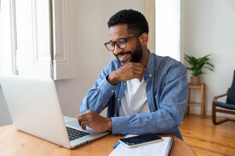Quais são os benefícios do programa | Homem sorrindo enquanto usa no notebook em casa | Minha Casa, Minha Vida | Blog da Tenda 