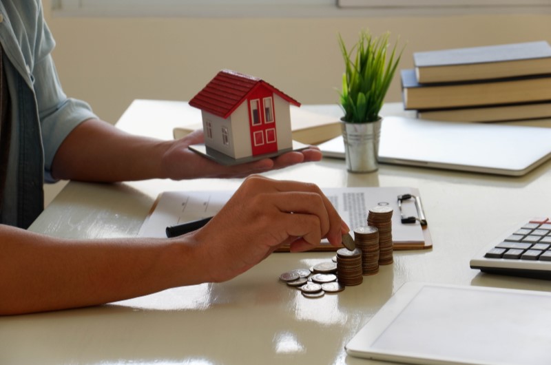 Quem tem direito ao programa habitacional | Pessoa segurando casa em miniatura e empilhando moedas | Minha Casa, Minha Vida | Blog da Tenda