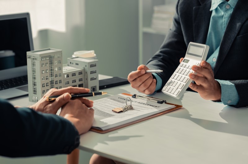 Vantagens da administradora de condomínio | Negociação com calculadora e contrato sobre a mesa | Viver em Condomínio | Blog da Tenda 