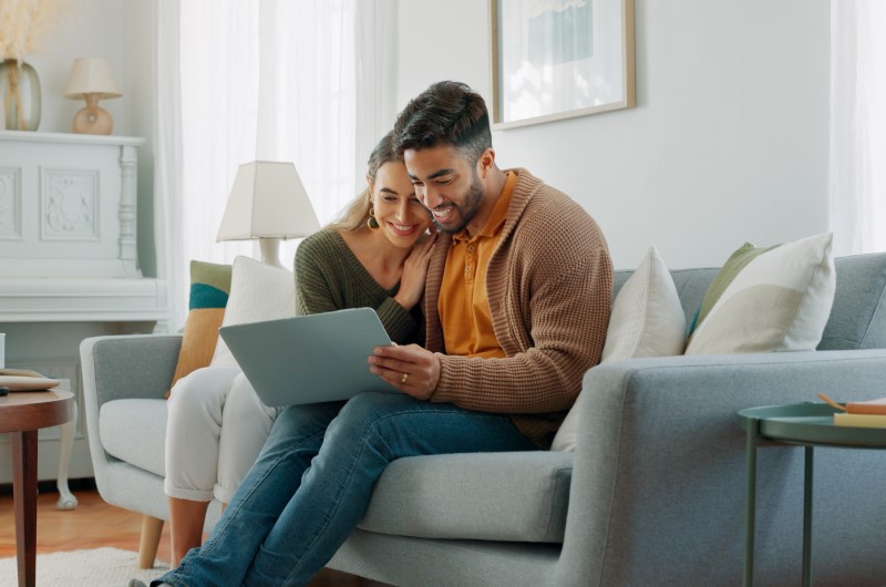 Moradia para pessoas de baixa renda | Casal usando notebook no sofá da sala | Trilha da Conquista | Blog da Tenda 