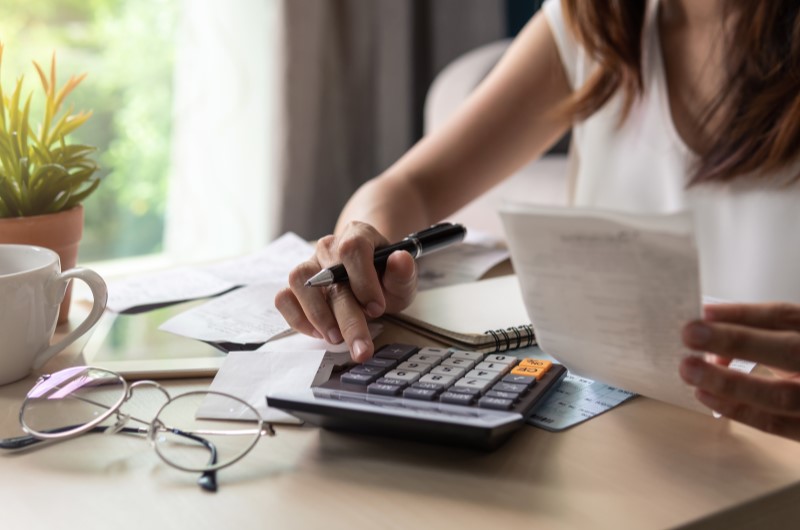 Planejamento financeiro | Foto de uma moça segurando um papel enquanto usa a calculadora | Dúvidas sobre dívidas | Eu Dou Conta