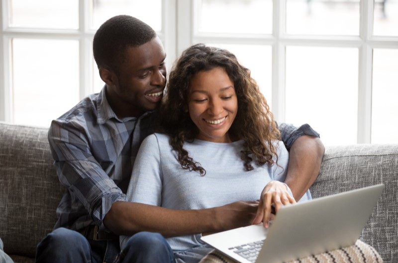 Casal sorridente mexendo no computador | O que é empréstimo consignado | Dúvida sobre dívidas 