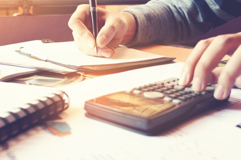 O que é financiamento | Foto de uma pessoa usando um caderno e calculadora | Dúvidas sobre dívidas | Eu Dou Conta