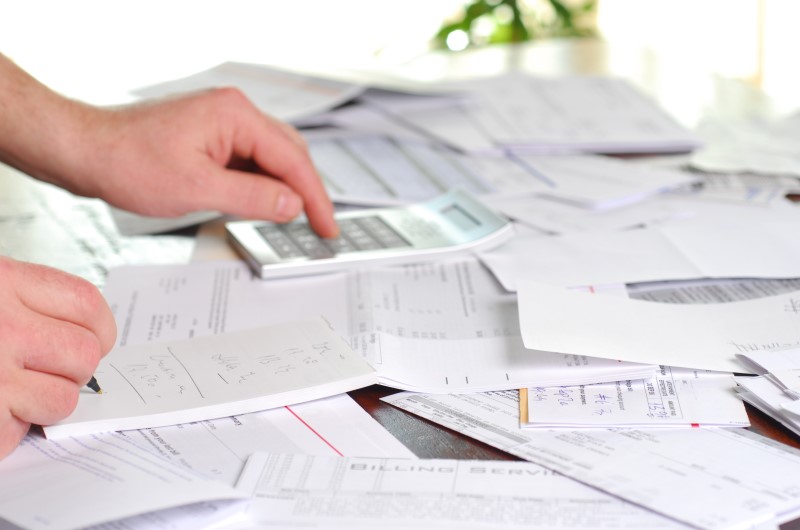 Tipos de dívidas | Foto de uma pessoa fazendo contas na calculadora em uma pilha de dívidas | Como limpar o seu nome | Eu Dou Conta
