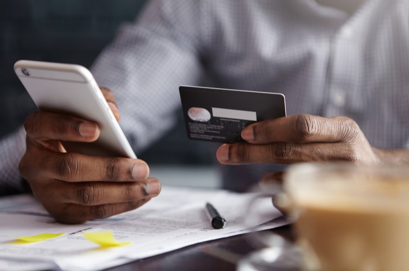 Tudo sobre contas bancárias | Homem segurando um cartão de crédito e um celular