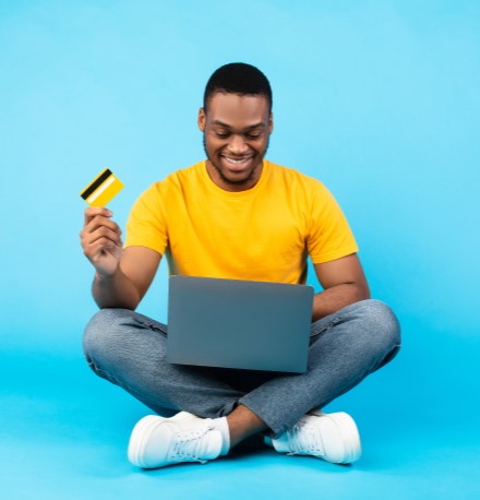 Como quitar dívidas | Homem jovem sentado segurando um cartão de crédito e pesquisando na internet | Dúvidas sobre dívidas | Eu Dou Conta