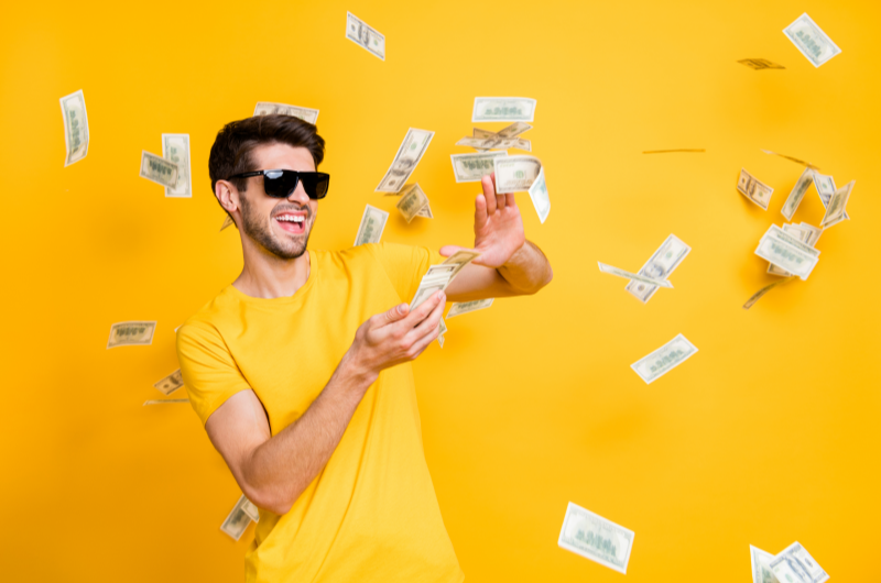 O que são gastos desnecessários | Foto de um homem feliz jogando notas de dinheiro para o ar | Economia e renda extra | Eu dou Conta