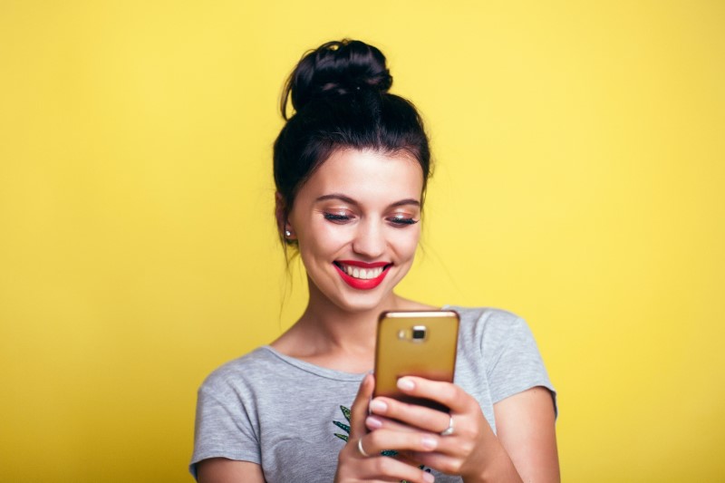 Como vender na Páscoa | Foto de ume mulher sorrindo pesquisando no celular | Economia e renda extra | Eu Dou Conta