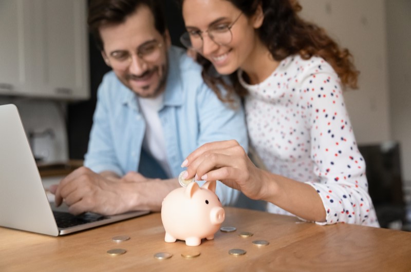 Como fazer um planejamento financeiro? | Foto de um casal sorridente colocando moedas em um cofrinho | Como limpar o seu nome | Eu Dou Conta
