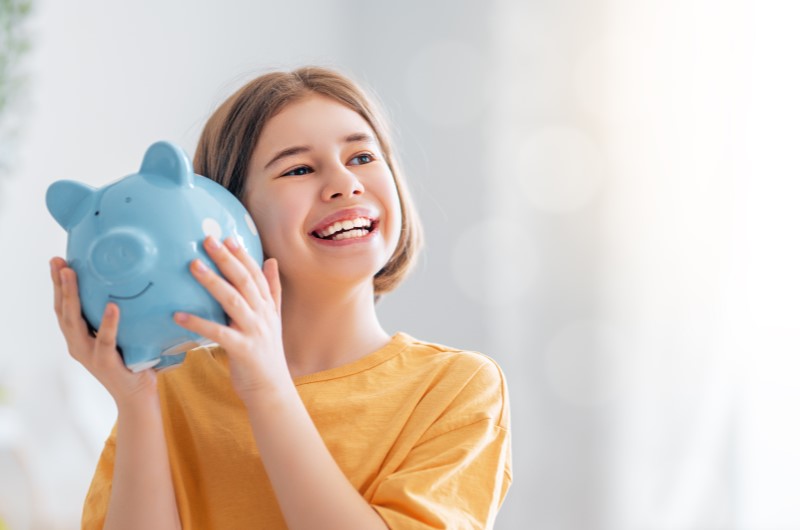 Qual a importância do planejamento financeiro | Foto de uma menina feliz segurando um cofrinho | Como limpar o seu nome | Eu Dou Conta