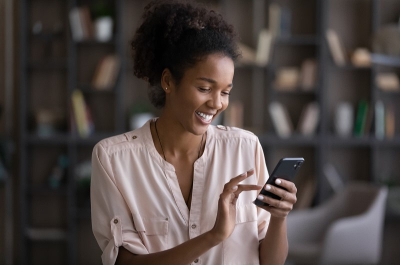 Como se tornar um afiliado Clickers? | Foto de uma muller sorrindo e utilizando o celular | Economia e renda extra | Blog Eu Dou Conta