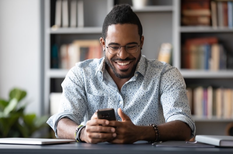 Crie um blog sobre um assunto que você domina | Foto de um homem sorridente utilizando o celular | Economia e renda extra | Blog Eu Dou Conta