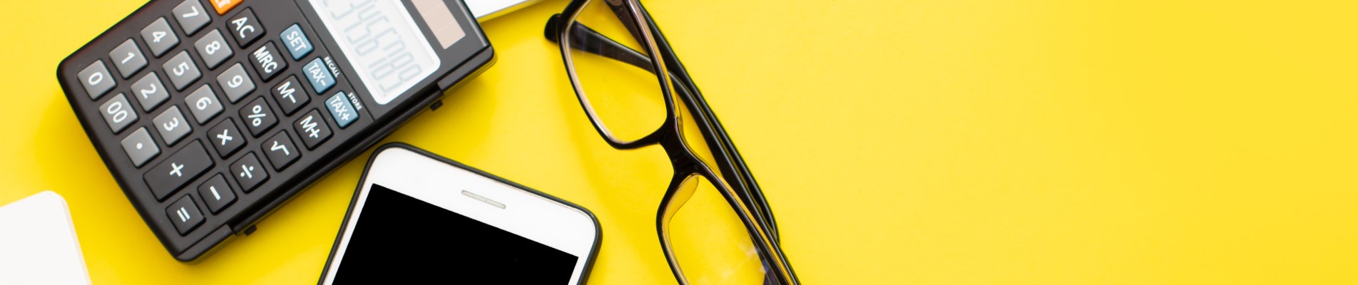 Desenrola Brasil: o que é, como funciona e como limpar o seu nome | Foto de um fundo amarelo, com um celular, óculos e calculadora | Como limpar o seu nome | Blog Eu Dou Conta