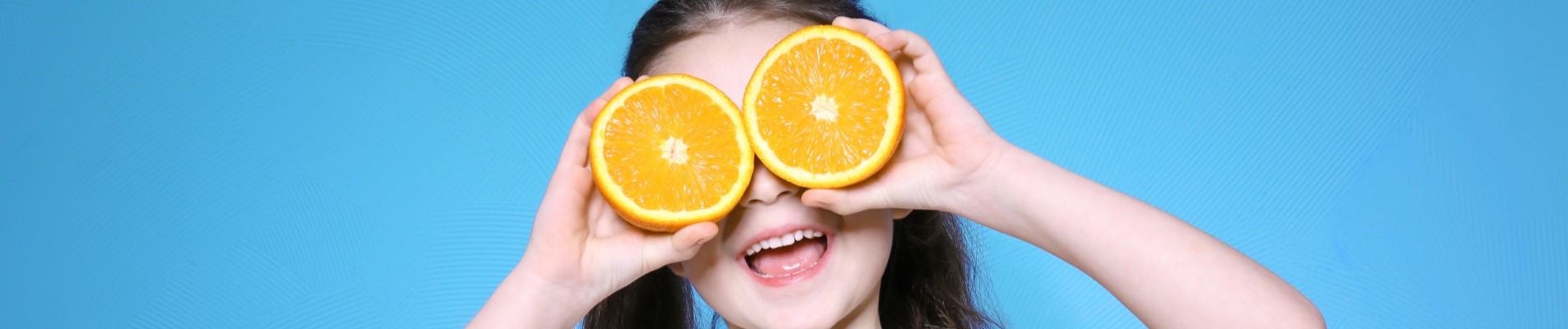 10 ideias para economizar nos presentes de Dia das Crianças | Foto de uma criança sorrindo enquanto segura duas laranjas em frente do rosto | Economia e renda extra | Eu Dou Conta