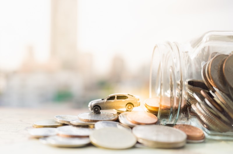 Financiamento de veículos | Foto de um pote de moedas caindo, com uma miniatura de carrinho em cima | Dúvidas sobre dívidas | Eu Dou Conta 