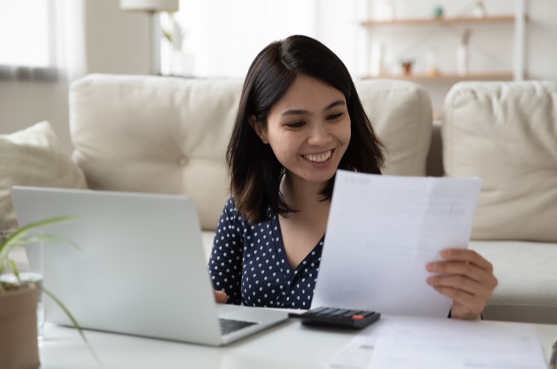 Arrojado | Foto de uma mulher sorrindo para um papel enquanto usa o notebook | Economia e renda extra | Eu Dou Conta 