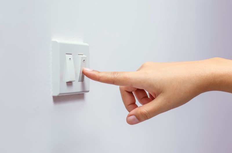 Evite deixar a luz acesa sem ninguém no local | Foto de uma pessoa pressionando o botão do interruptor de luz | Economia e renda extra | Eu Dou Conta 