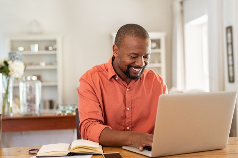 O que é trabalho autônomo? | Foto de um homem sorrindo enquanto utiliza um notebook | Economia e renda extra | Eu Dou Conta 