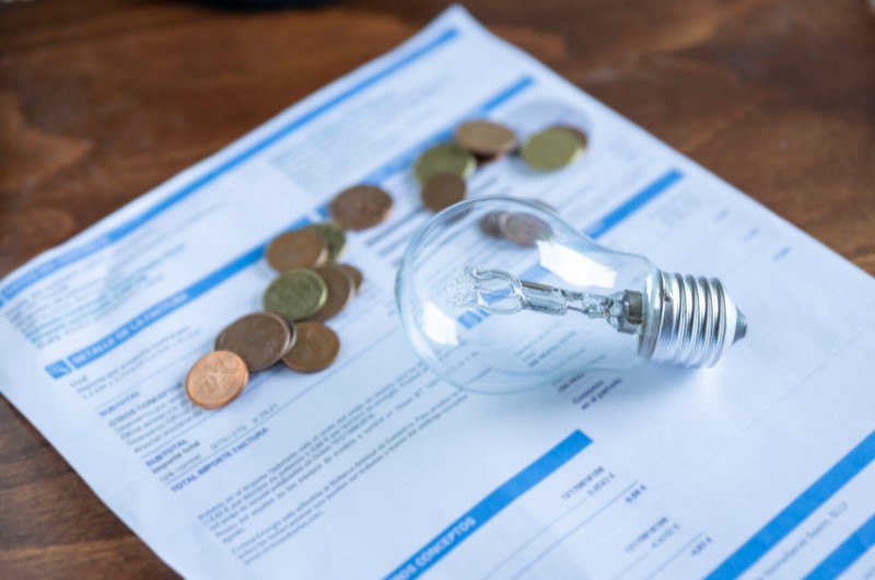 Tire os aparelhos da tomada | Foto de uma conta de energia, com algumas moedas e uma lâmpada em cima | Economia e renda extra | Eu Dou Conta 