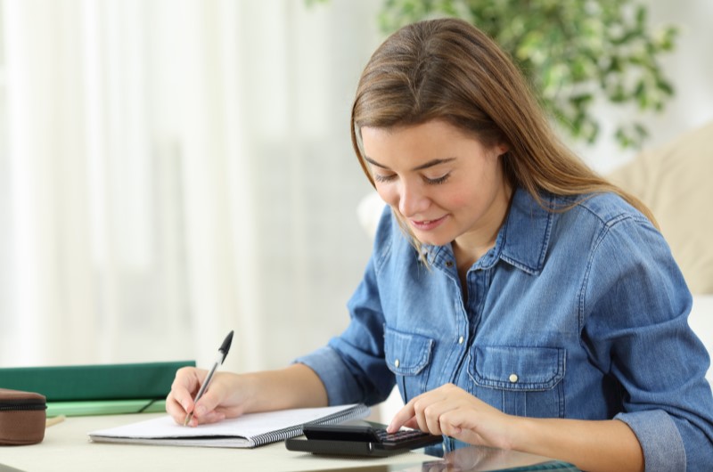 Como fazer um orçamento financeiro para o próximo ano? | Foto de uma mulher usando a calculadora e escrevendo em um caderno | Economia e renda extra | Eu Dou Conta 