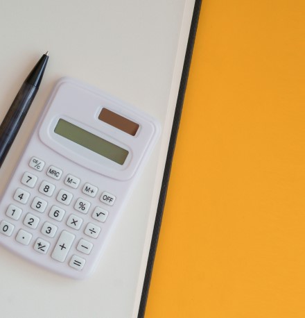 Despesas fixas e variáveis: veja o que são e como organizá-las | Foto de uma calculadora e caneta sobre um caderno | Economia e renda extra | Eu Dou Conta