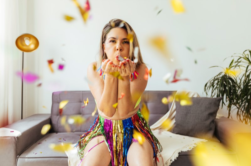 O que é o Carnaval? | Foto de uma pessoa soprando confetes, com uma fantasia de Carnaval | Economia e Renda Extra | Eu Dou Conta 