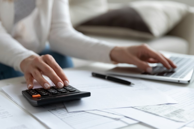 O que são despesas variáveis? | Foto de uma pessoa usando uma calculadora e um notebook, com diversos papéis sobre a mesa | Economia e renda extra | Eu Dou Conta 