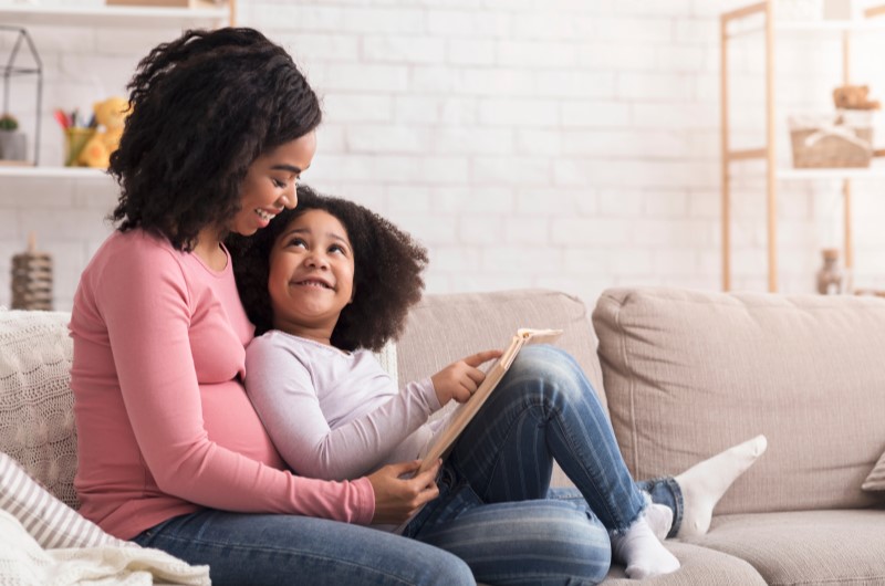 11 dicas de educação financeira para crianças | Foto de uma mãe e filha lendo um livro na sala de estar | Economia e renda extra | Eu Dou Conta 