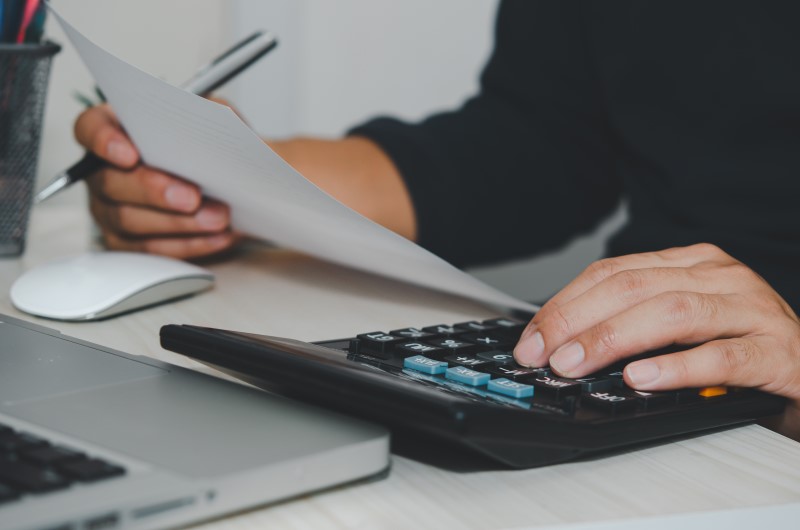 O que é finanças pessoais? | Foto de uma pessoa digitando na calculadora e segurando um papel | Economia e renda extra | Eu Dou Conta 