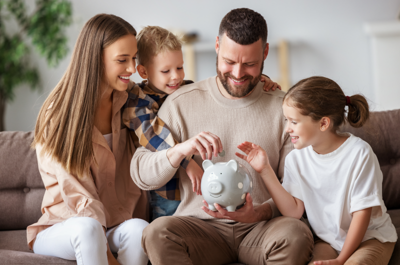 13 dicas de como fazer um orçamento familiar | Foto de uma família na sala de estar, colocando moedas em um cofrinho | Economia e Renda Extra | Eu Dou Conta 