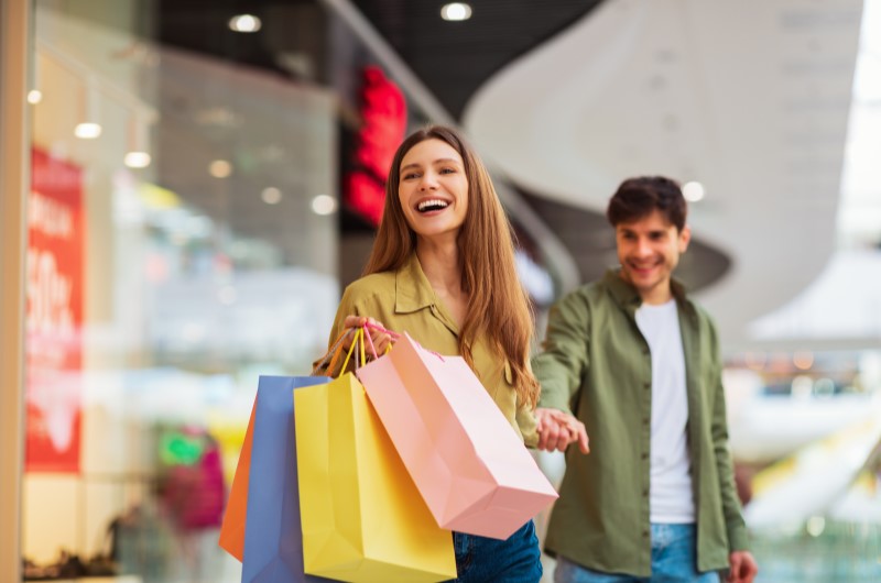 14 dicas de como evitar comprar por impulso | Foto de um casal sorridente no shopping, com diversas sacolas de compra | Economia e renda extra | Eu Dou Conta 